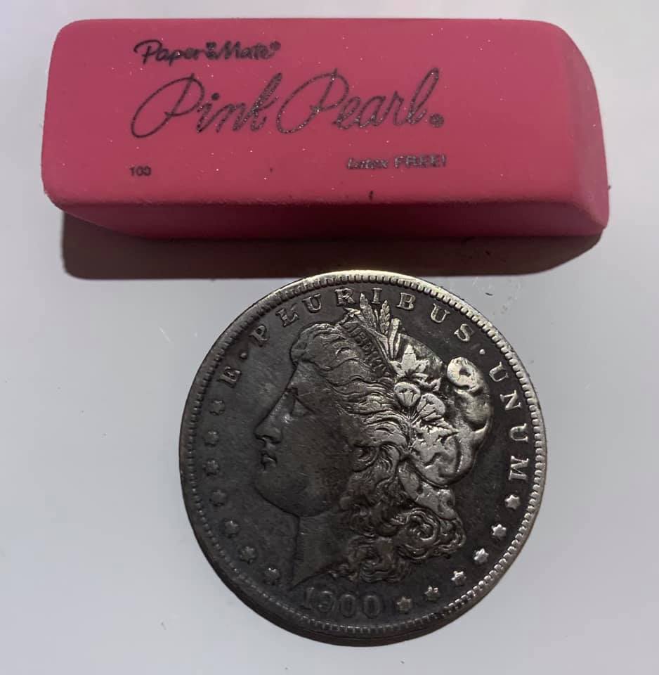 Using a pink eraser to clean the raised surfaces of a darkened coin